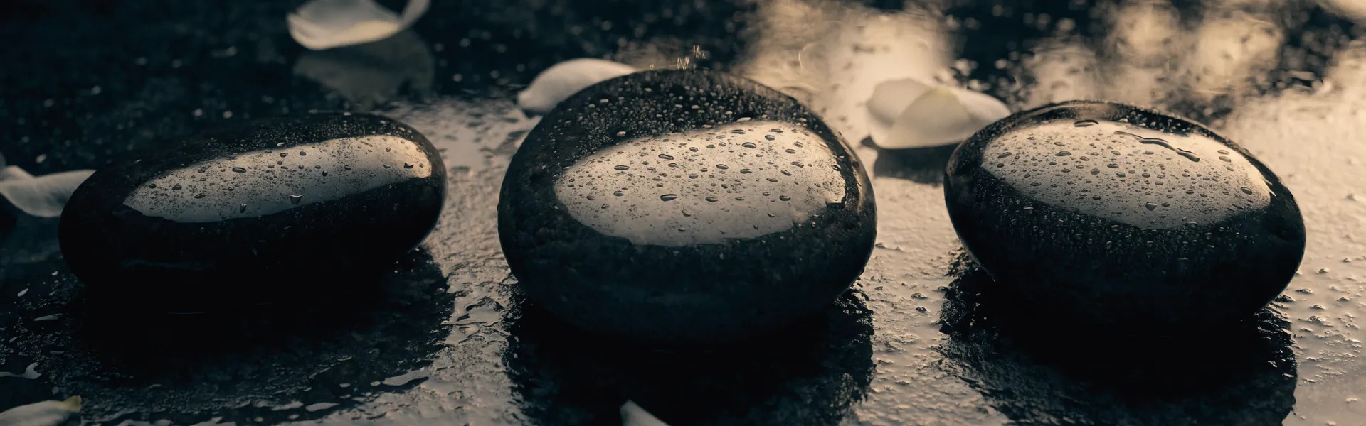 Piedras de masaje mojadas y pétalos blancos con luz cálida